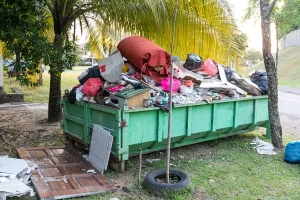 A green container overflowing with trash beside the street