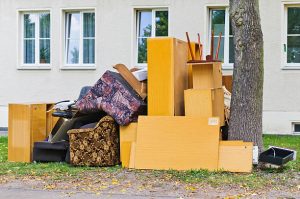 Bulky waste including an old couch and cabinets outside the house beside the tree.